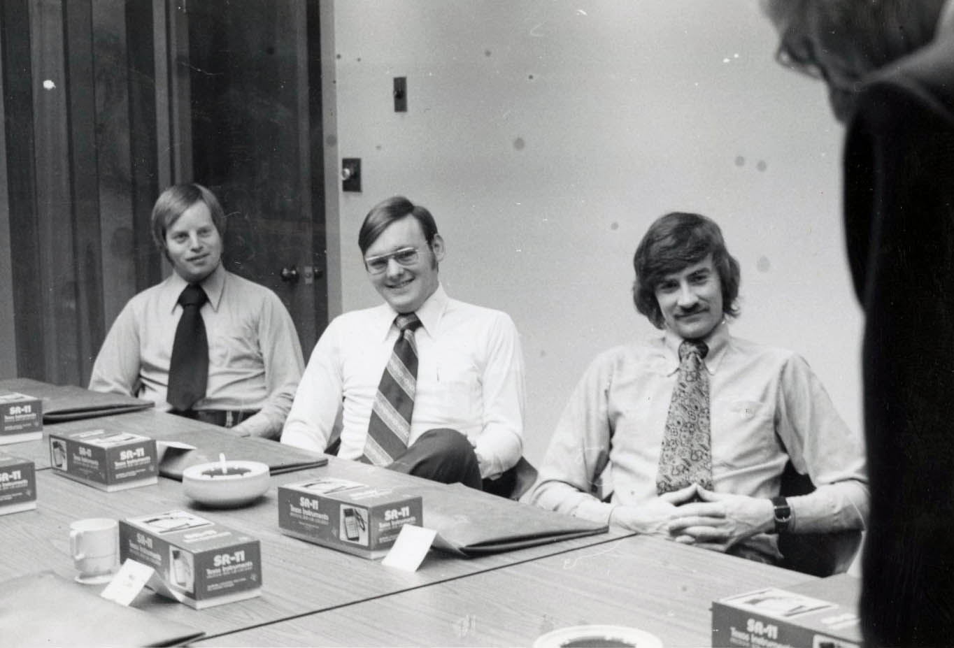 An archival photo from 1975 showing Kurt Polsley seated on the far left next to two other men in a sales meeting.